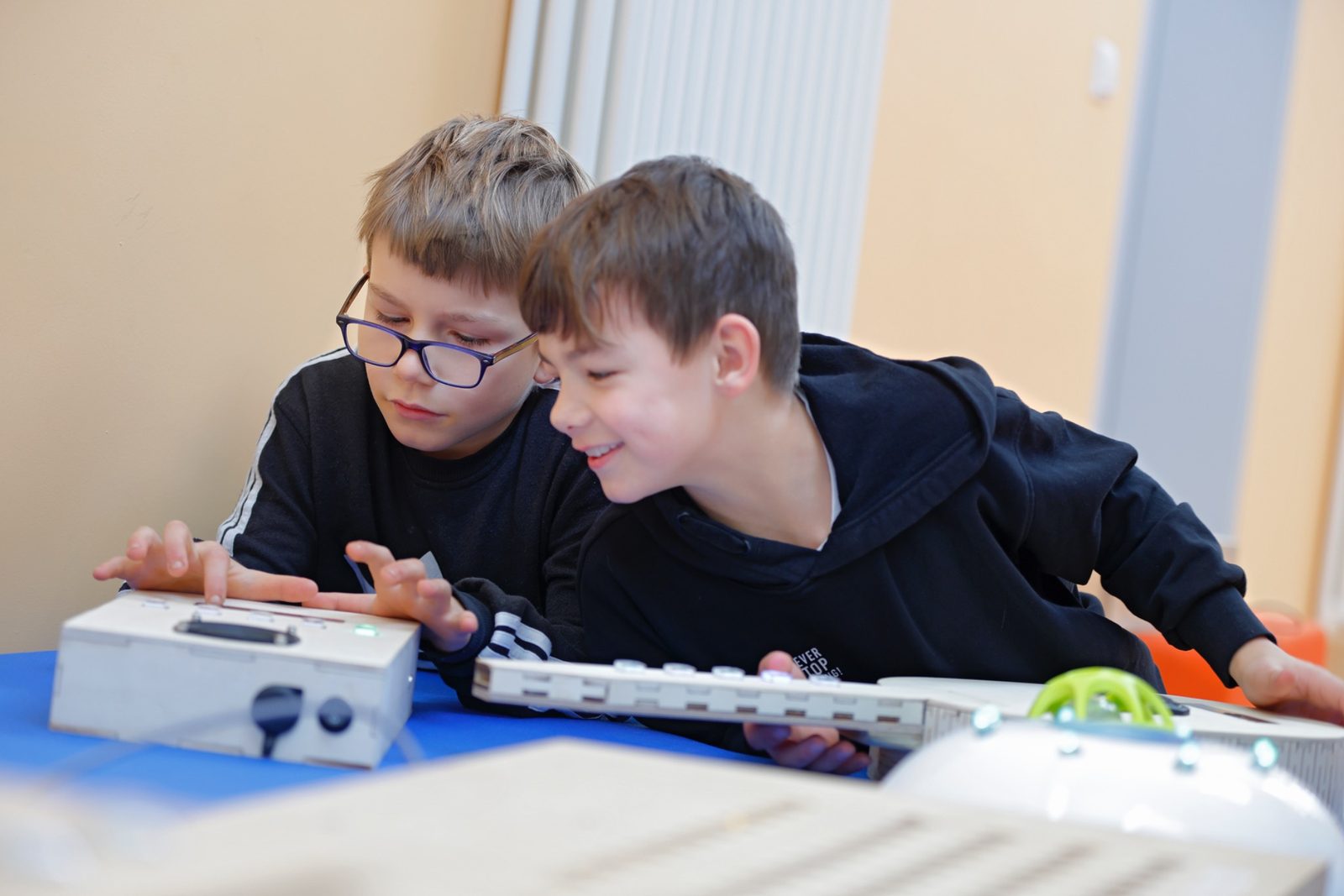 Zwei Kinder spielen auf zwei digitalen Musikinstrumenten, eines in Gitarrenform und eines in kompakter Bauweise.